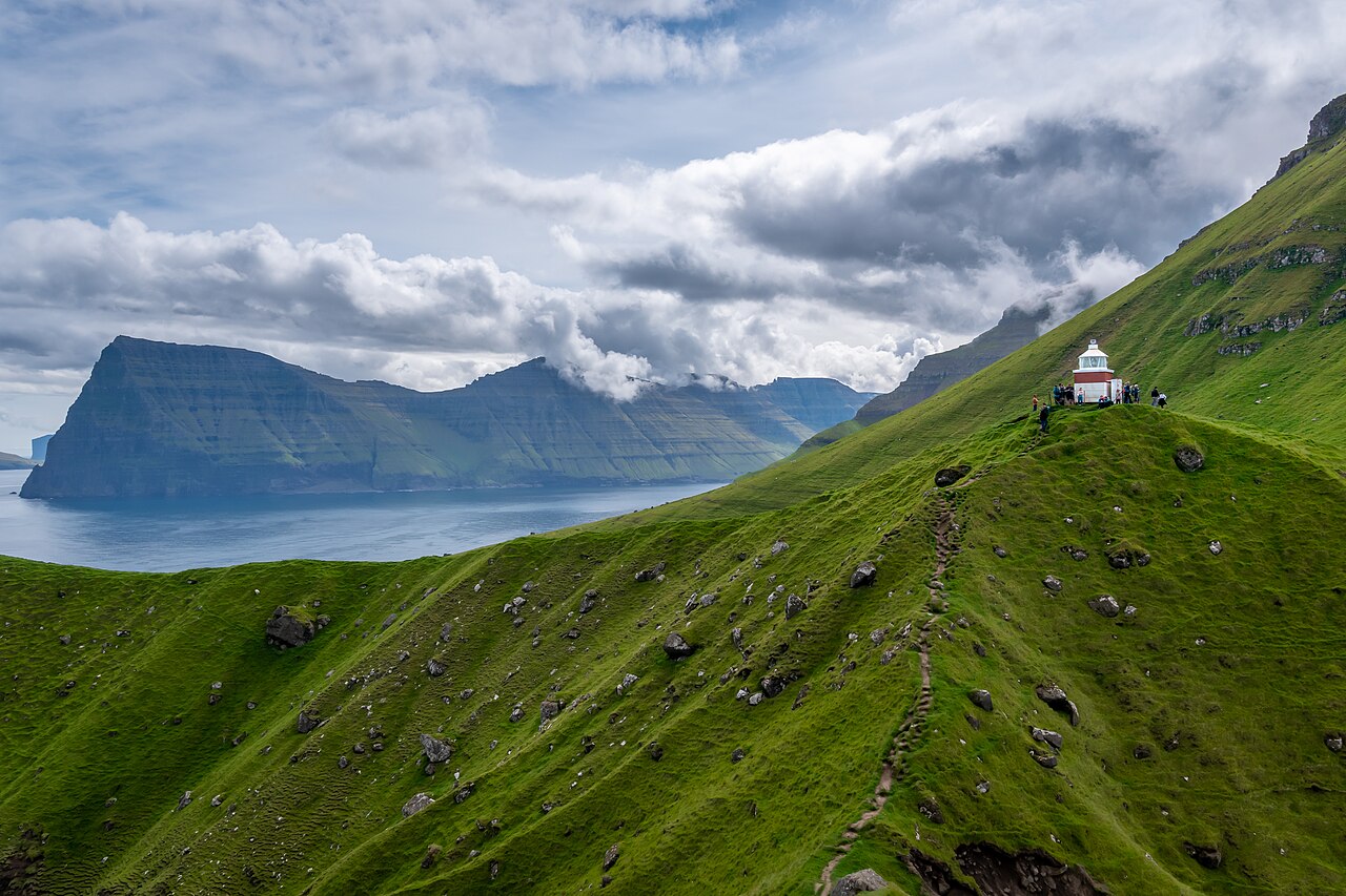 Kallur fyr på en smal græsklædt klippetange yderst på Kalsoy med havet omkring